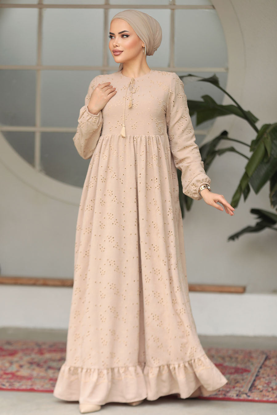 Muslim woman wearing a beige embroidered cotton maxi dress with ruffle hem and long sleeves, modest and breathable for casual or formal wear.