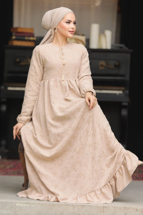 Muslim woman wearing a beige embroidered cotton maxi dress with ruffle hem and long sleeves, modest and breathable for casual or formal wear.