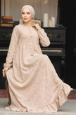 Muslim woman wearing a beige embroidered cotton maxi dress with ruffle hem and long sleeves, modest and breathable for casual or formal wear.